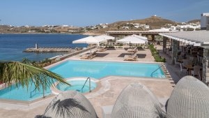 foto ausblick über den aussenbereich des resorts mit pool und jakuzzi whirlpool daneben eine terrrasse mit sonnenliegen und ein restaurant überdacht auf der anderen seite das azur blaue meer und im hintergrund hügel mit weissen häusern darauf im luxuriöse
